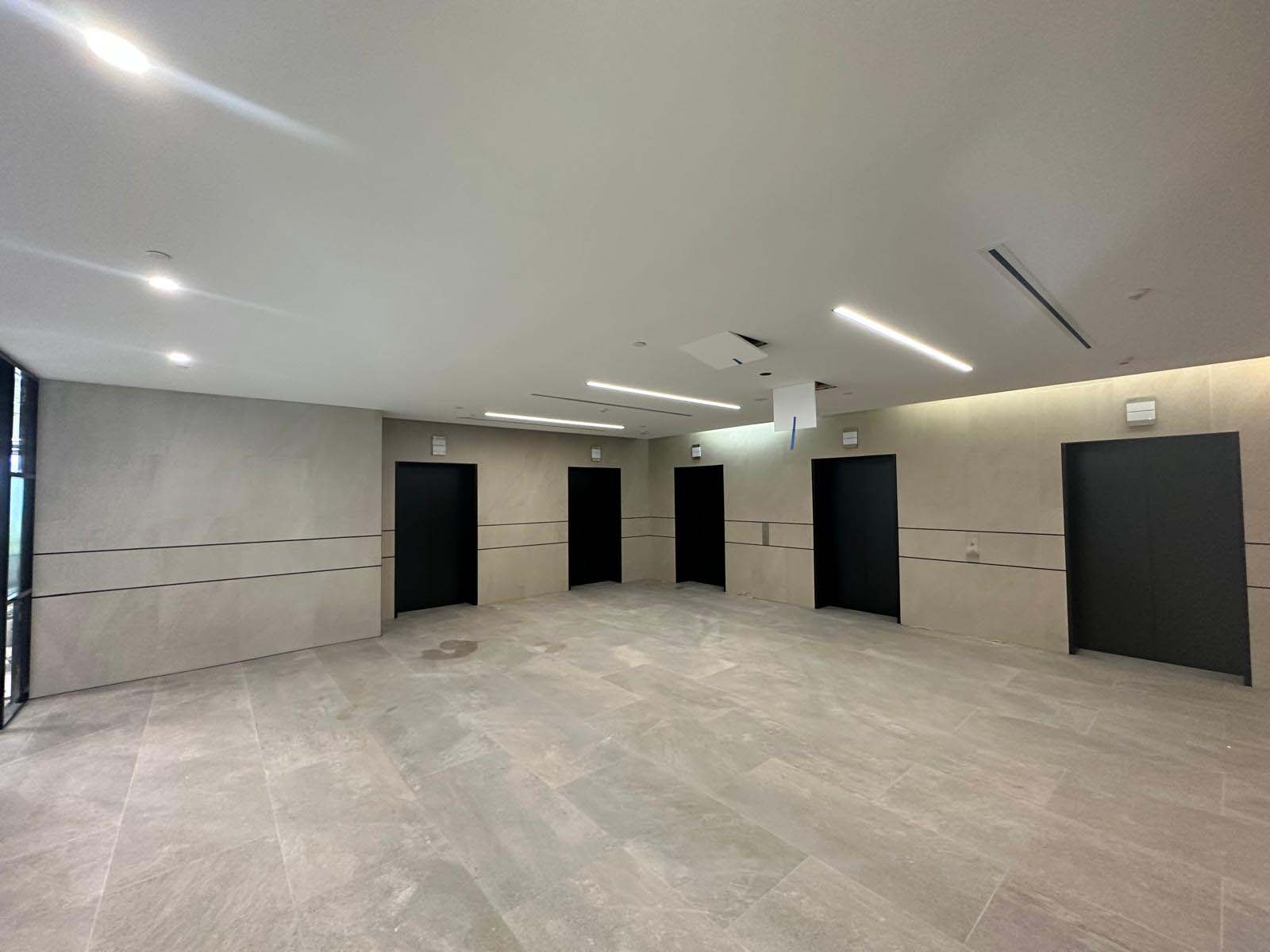 Spacious foyer with large-format grey floor and wall tiles and black doors