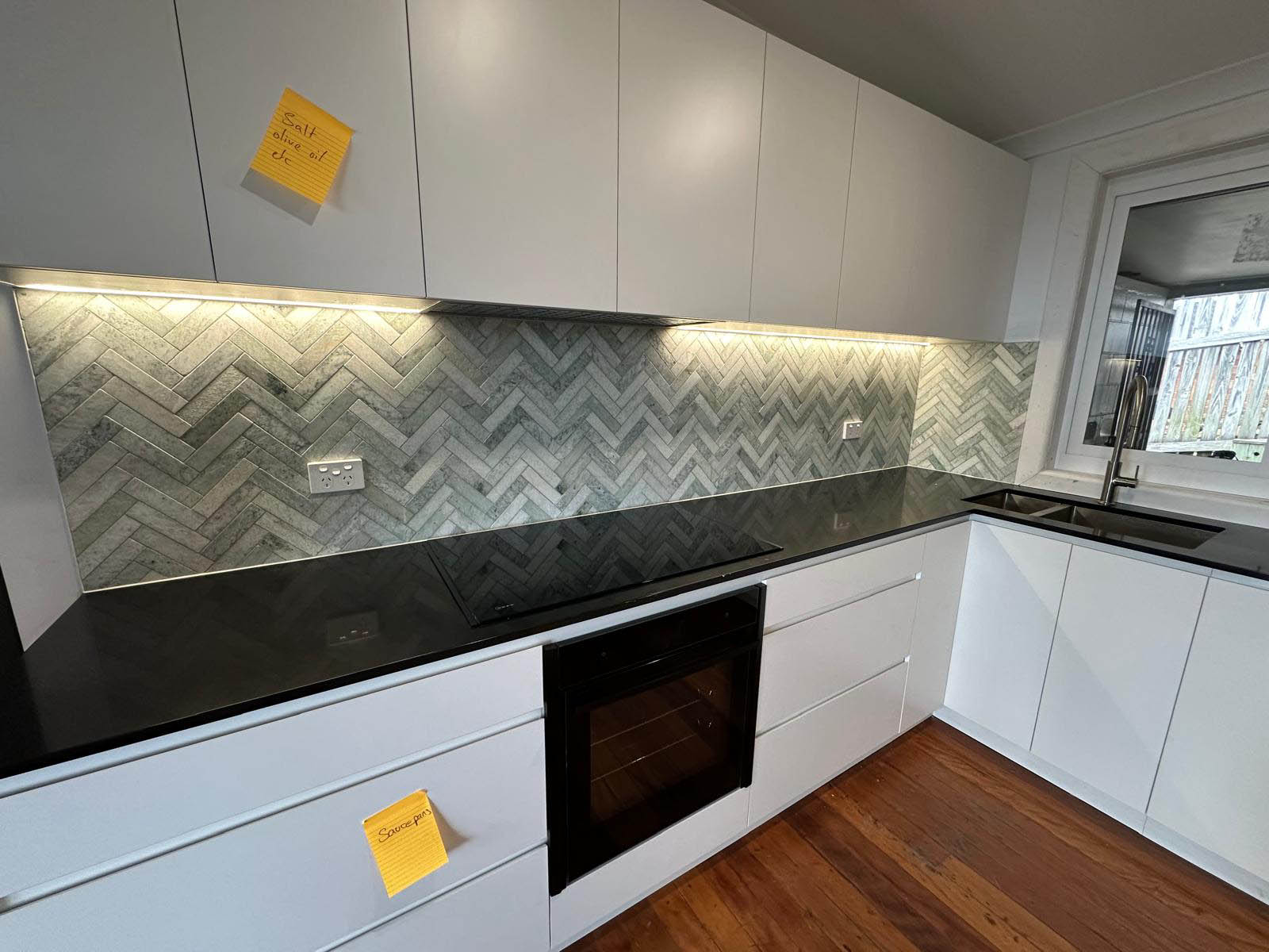 Kitchen with a green-grey herringbone tile splashback above a black benchtop