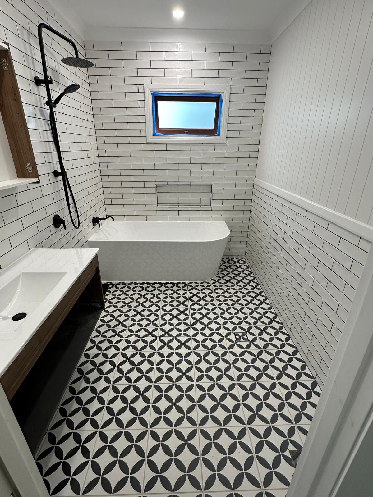 Bathroom with black and white patterned floor tiles, freestanding bath and white subway tiles